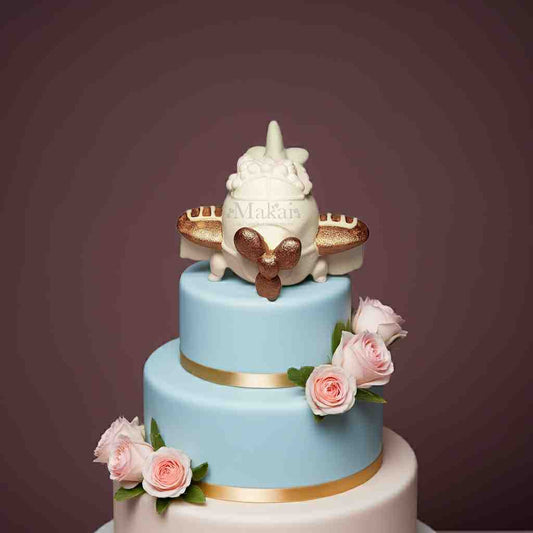 Gold and white fondant airplane cake topper placed on a blue and white tiered cake decorated with pink roses and golden ribbons.