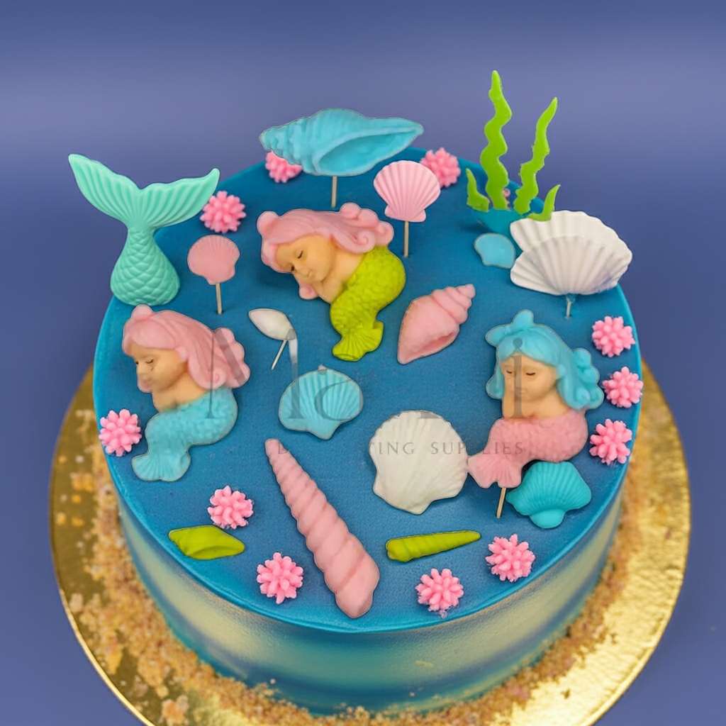 Blue ocean-themed cake decorated with pastel mermaid toppers, seashells, seaweed, and coral accents — part of the Mini Mermaid Cake Topper Set from Makai Cake Decorating Supplies.