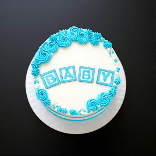 Baby shower cake with blue frosting decorations, pearls and BABY letter blocks on white icing.