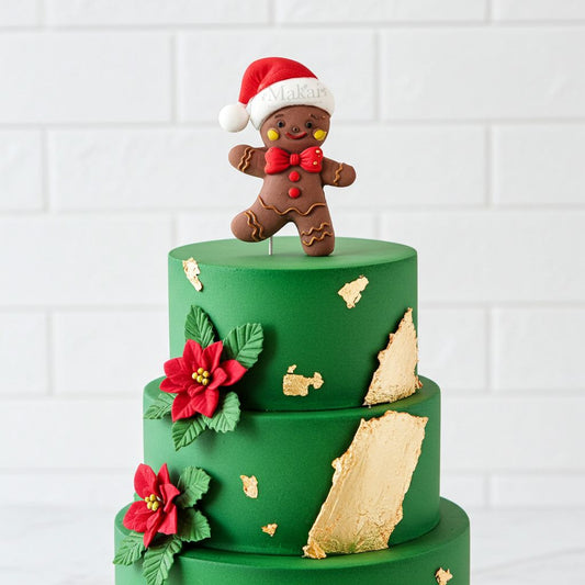 Festive gingerbread man Christmas cake topper displayed on a green three-tier cake with poinsettia decorations and gold leaf accents