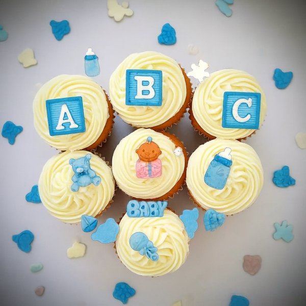 Baby shower cupcakes decorated with blue fondant toppers, including ABC blocks, teddy bear, baby bottle and baby accessories.