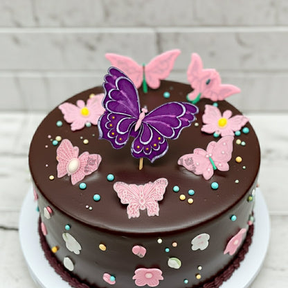 Chocolate cake decorated with edible pink and purple butterfly toppers and pastel sugar sprinkles.