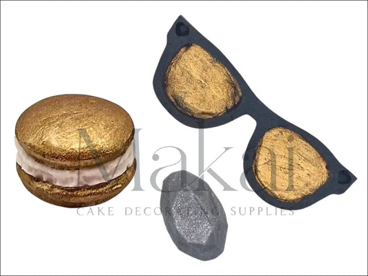 Black heart-shaped sunglasses with gold lenses, a gold macaron, and a shimmering grey diamond-shaped fondant cake decoration.