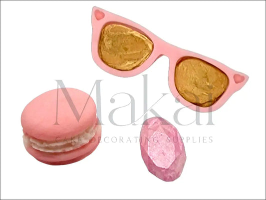 Pink heart-shaped sunglasses with gold lenses, a pink macaron, and a shimmering pink diamond-shaped fondant cake decoration.