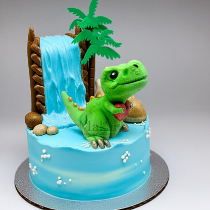 Blue cake with a waterfall and palm tree, decorated with a green fondant dinosaur holding a red heart.