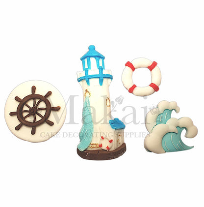 White and blue fondant lighthouse cake topper set with waves, lifebuoy, and ship wheel decorations.