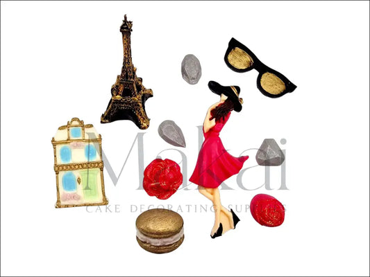 Paris-themed fondant cake decoration set with Eiffel Tower, Parisian building, stylish woman, macaron, sunglasses, roses, and gems.