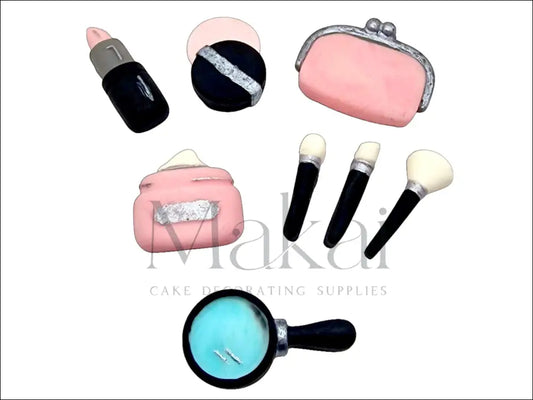 Pink fondant makeup set with brushes, mirror, wallet, cream, and lipstick for cake decoration.