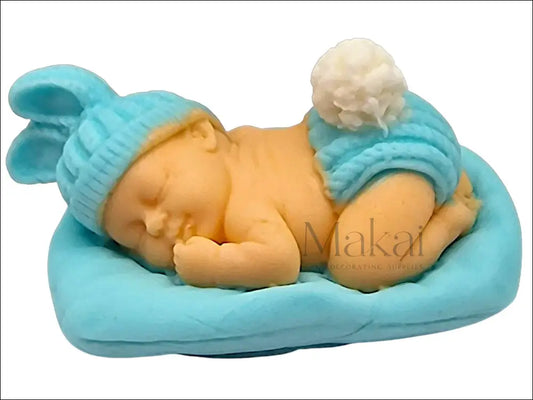Sleeping baby cake decoration in blue, resting on a matching blue pillow with a hat and diaper.