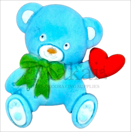 Edible baby blue teddy bear cake topper with red heart and green bow.
