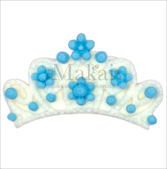 White baby crown cake topper decorated with blue pearls and flower accents.