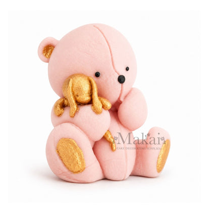 Baby pink teddy bear fondant cake topper holding a gold bunny decoration, side view
