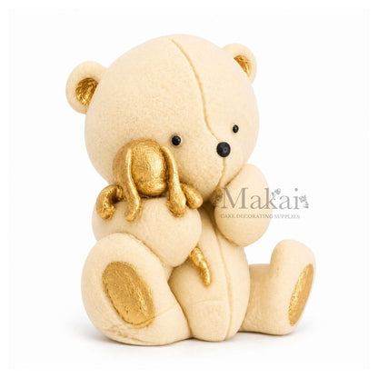 Beige teddy bear fondant cake topper holding a gold bunny decoration, side view