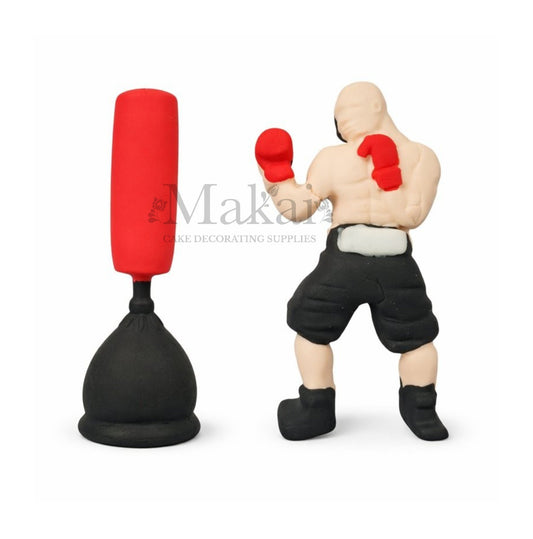 Boxer figurine with red boxing gloves and black shorts next to a punching bag on a white background. Cake Decoration
