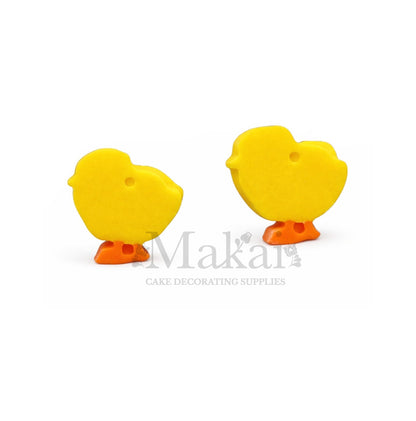 Two yellow duck-shaped cake decorations with orange feet on a white background, branded 'Makai'.