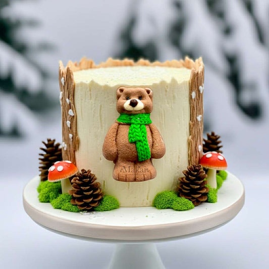 Winter forest-themed cake featuring a cute fondant bear wearing a green scarf, surrounded by pine cones and mushrooms on a snowy base.