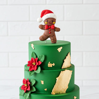 Festive gingerbread man Christmas cake topper displayed on a green three-tier cake with poinsettia decorations and gold leaf accents