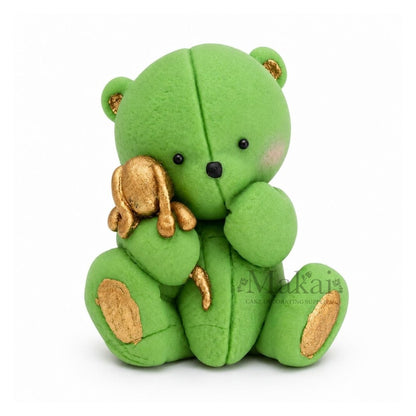 Green teddy bear fondant cake topper holding a gold bunny decoration, front view