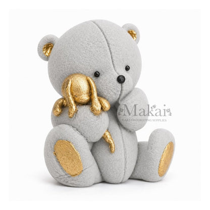 Grey teddy bear fondant cake topper holding a gold bunny decoration, side view