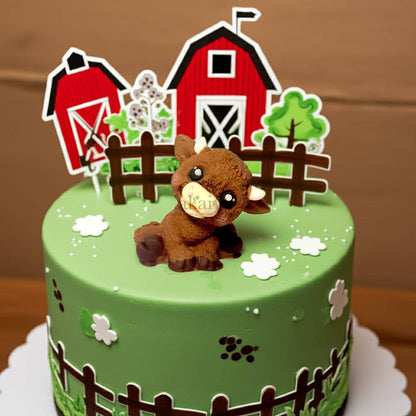 Edible Highland cow cake topper made from sugar paste, placed on a green farm-themed cake with barn and fence decorations – perfect for rustic birthday cakes.