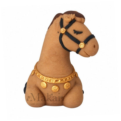 Handmade lying fondant horse cake topper with brown mane, black saddle and gold harness details, front view.