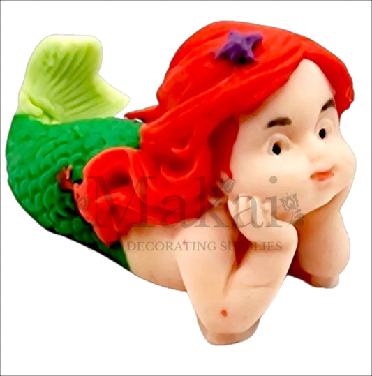 Lying mermaid baby edible cake topper with green tail and red hair, ideal for ocean and fantasy-themed cakes.