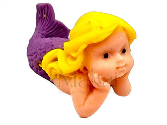  Blonde fondant mermaid girl lying on her stomach, with lilac tail, resting her face in her hands.