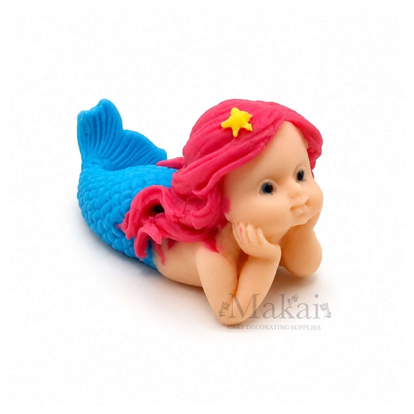 Pink fondant mermaid girl lying on her stomach, with blue tail, resting her face in her hands.