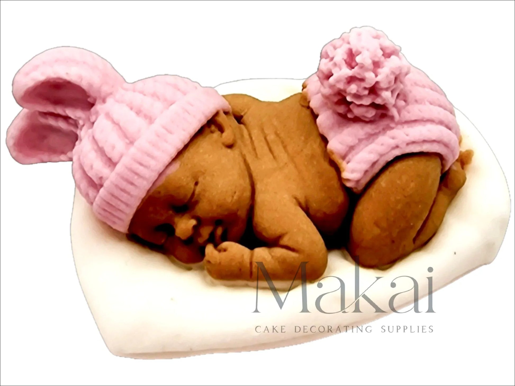 Darker-skinned fondant sleeping baby cake topper with a pink hat and little briefs, lying on a white pillow.