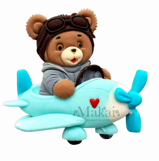 Fondant teddy bear pilot sitting in a blue airplane with goggles and detailed handcrafted features.