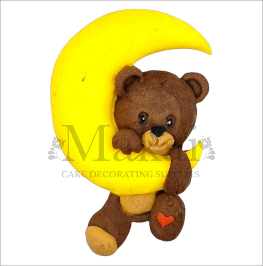 Edible cake topper of a brown teddy bear holding a crescent moon with a small red heart on its foot.