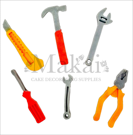 Edible cake toppers shaped like a hammer, screwdriver, utility knife, wrench, pliers, and spanner in grey, orange, and red.